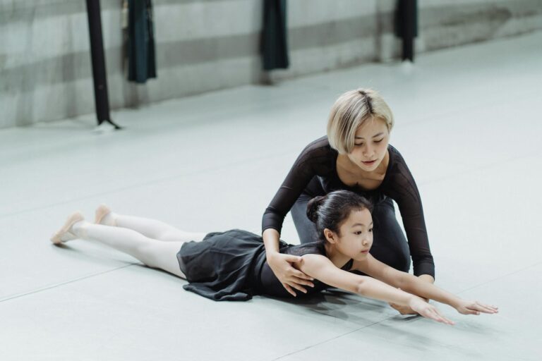 Ballet instructor helps a young dancer with stretching technique in a dance studio.
