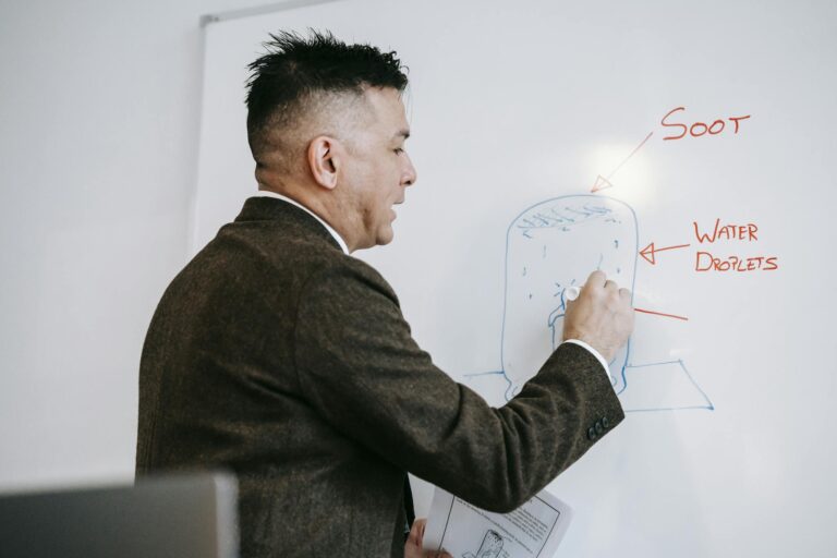 A male professional explains a diagram on a whiteboard during an educational session indoors.