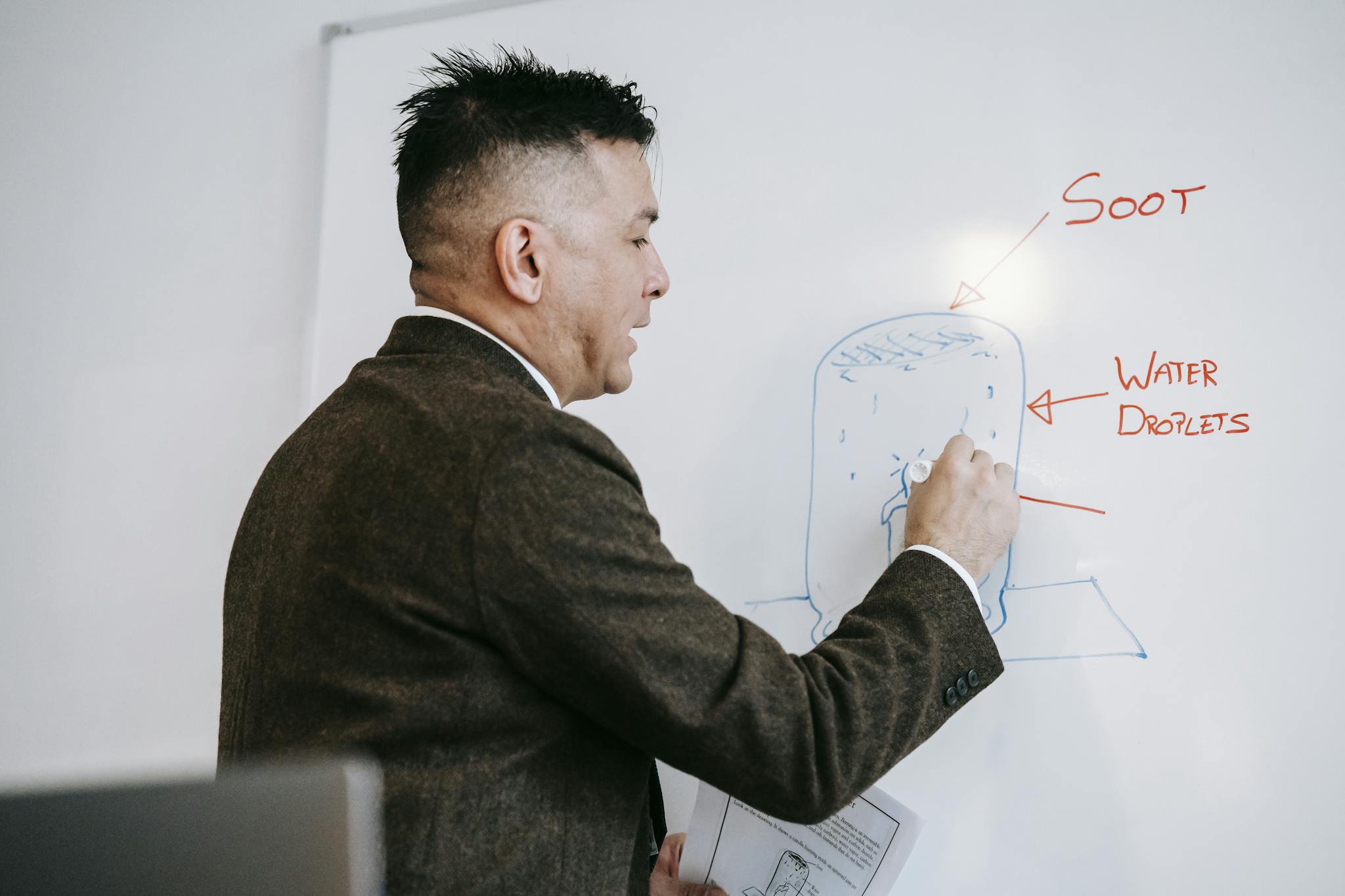 A male professional explains a diagram on a whiteboard during an educational session indoors.